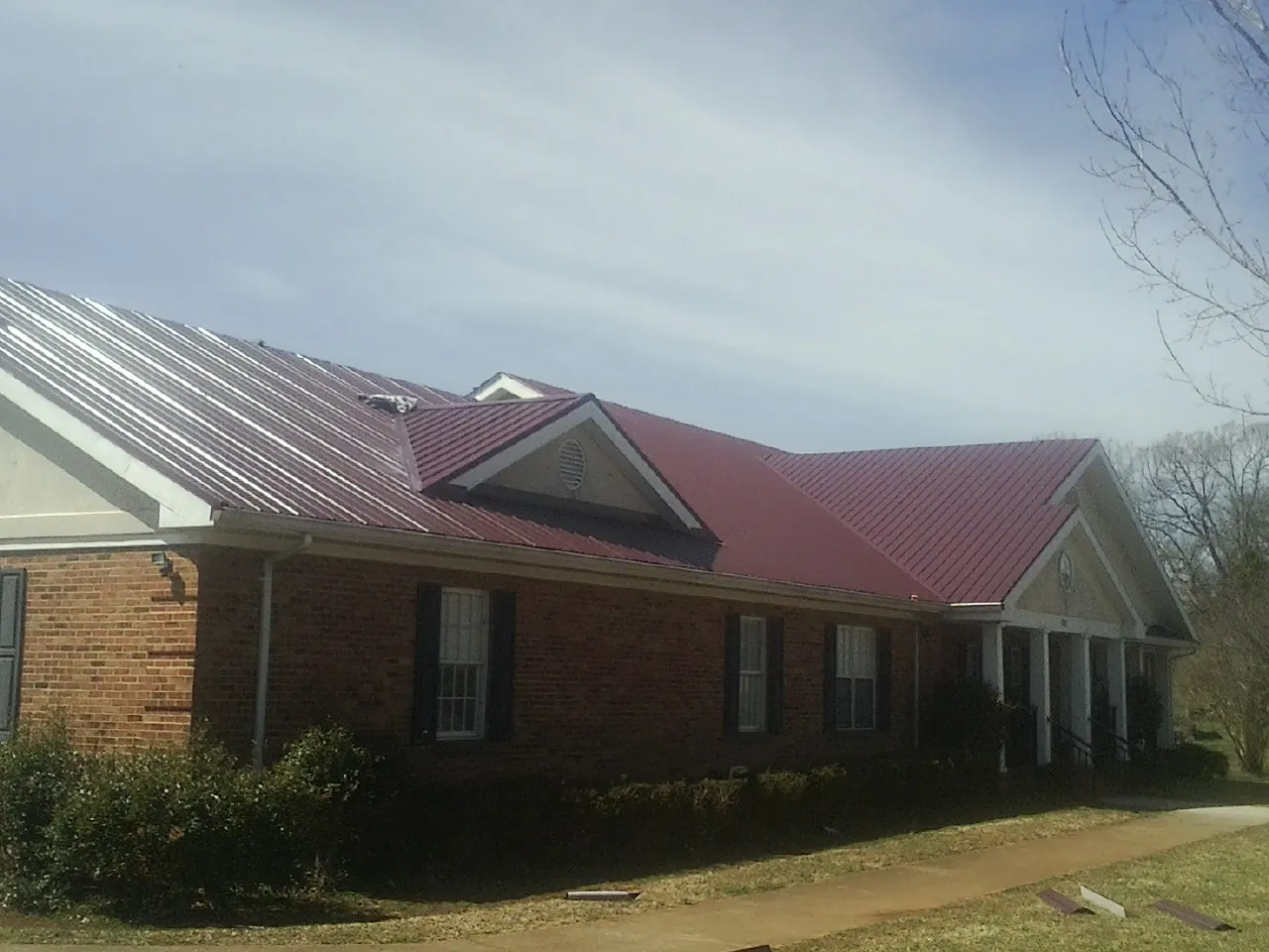Red metal roof with gabled entries on a long brick building, from a Hail Damage Roof Repair job in Oregon